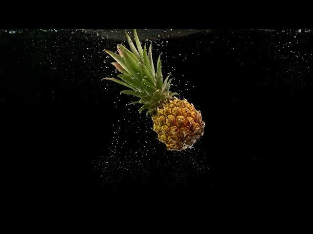 Tropical Fruit Pineapple Rotating and Falling Into Water with Splash Bubbles on Black Background