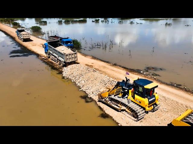 Strong Machinery Repairing Road On Water. Shantui Bulldozer And Large Dump Trucks Unloading Rock