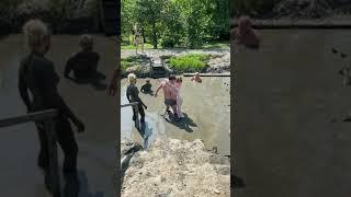 Man helps a disabled woman into a mud bath.