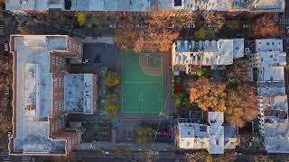 Aerial view revealing schoolyard and playground amid New York City neighborhood, surrounded by fall